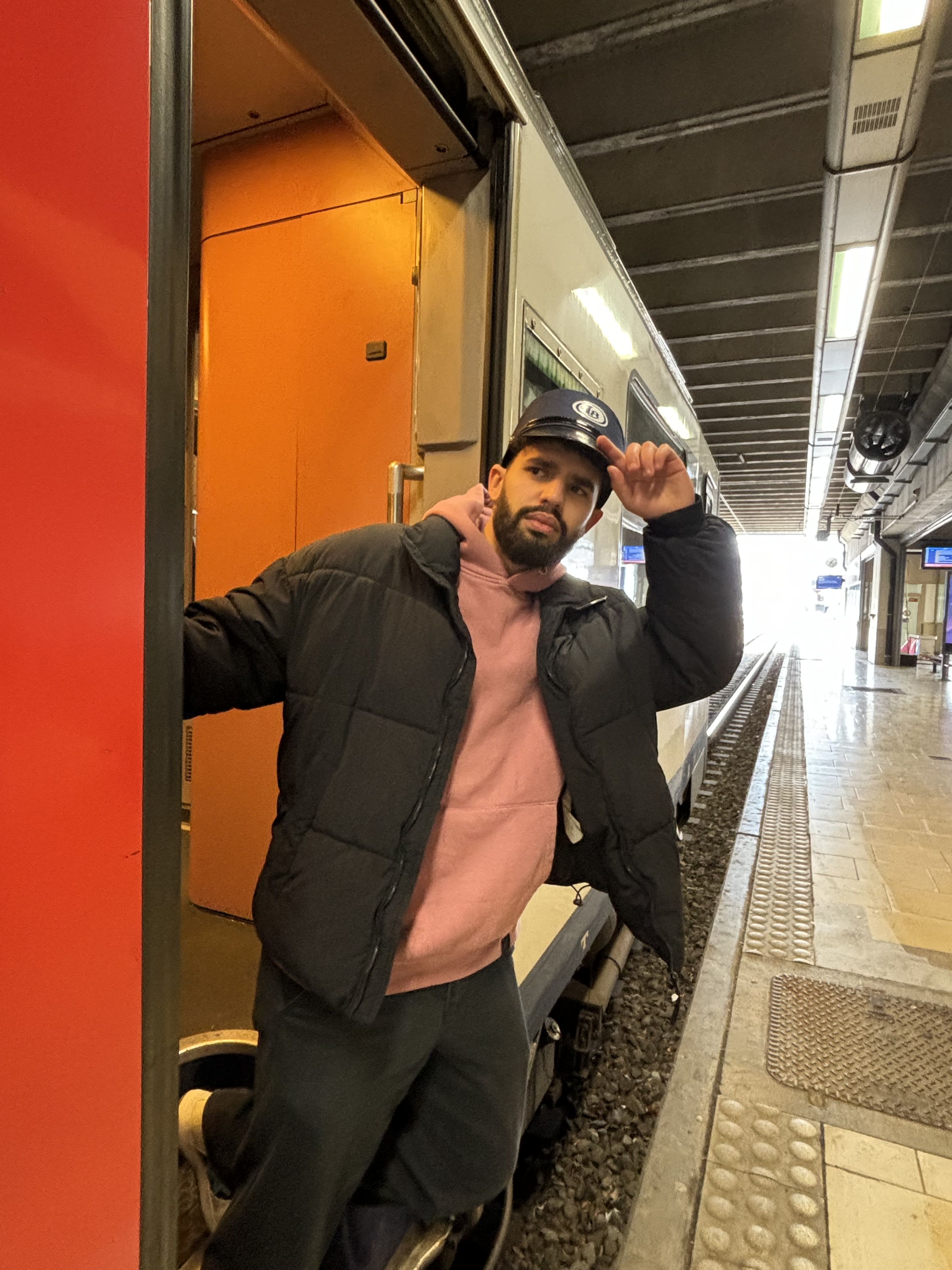 Photo de Fayssal, à l'entrée du train. Il est dans les escaliers et tient son képi posé sur sa tête.