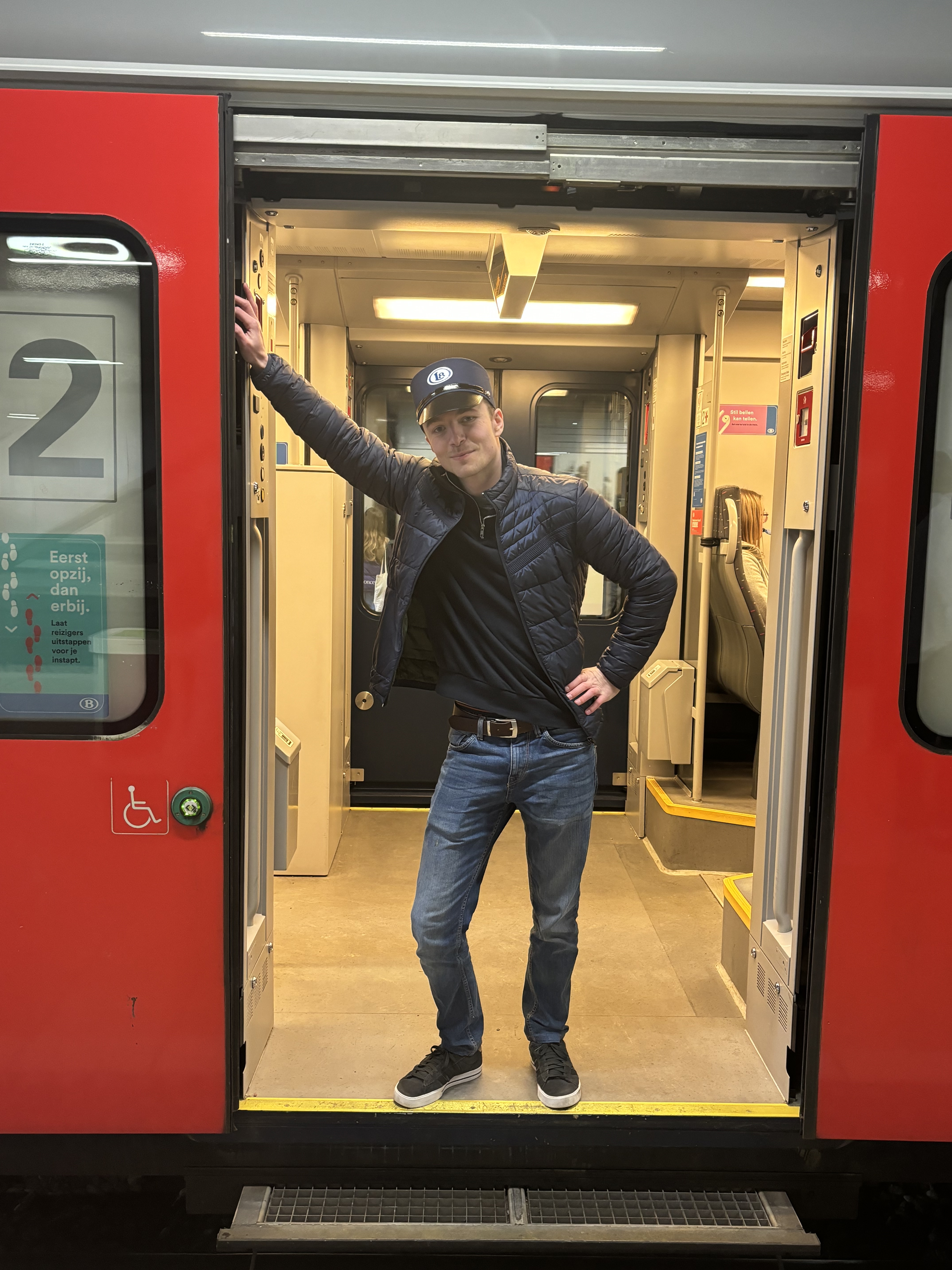 Photo de Jules à l'entrée d'un train. Il porte un képi avec le logo Late, une main pausée sur ses hanches, l'autre appuyée sur la porte.